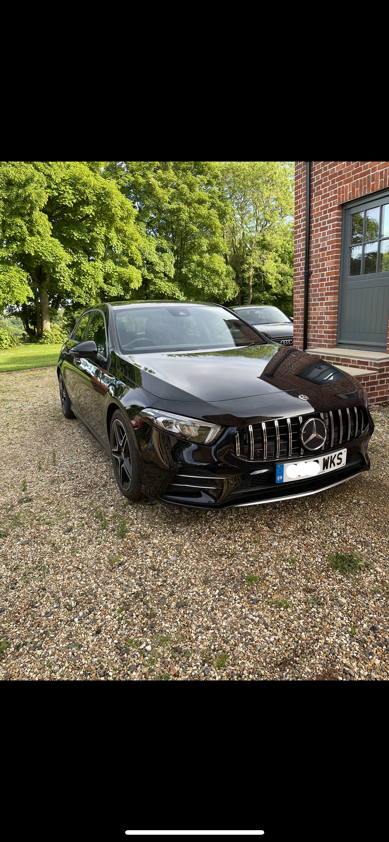Black Mercedes-Benz car parked on a gravel driveway with trees and a building in the background.